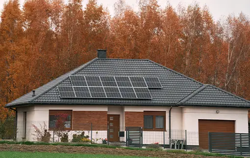 Nowoczesny parterowy dom z panelami fotowoltaicznymi zamontowanymi na ciemnym dachu, w tle jesienny las