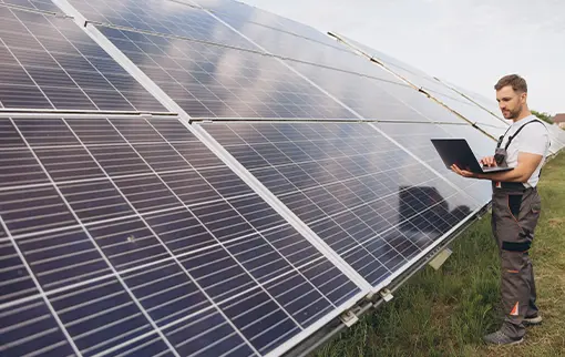 serwisant w stroju roboczym z laptopem sprawdza gruntową instalację fotowoltaiczną