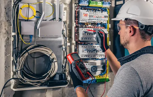 Elektryk w kasku używa multimetru do sprawdzenia otwartej rozdzielnicy elektrycznej